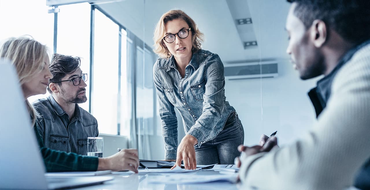 Mitarbeiterin beugt sich über einen Tisch und erklärt Kollegen eine neue Strategie